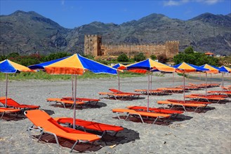 Colourful beach chairs and umbrellas in front of Frangokastello castle