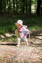 Toddler with doll and walking stick hiking through the woods
