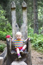 Toddler sitting on a big wooden chair in the forest