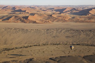 Hot-air balloon above an arid plain and the dry riverbed of the Tsauchab river at the edge of the Namib Desert