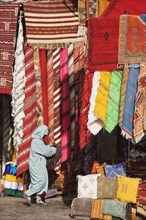 Woman in front of a shop with colourful carpets in the souks of Marrakesh