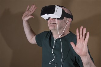 Man wearing ZEISS VR ONE virtual reality VR plastic goggles with bracket for Samsung Galaxy S5 Android smartphone and in-ear headphones