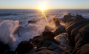 Breakwater on the rocky coast in the evening light with setting sun