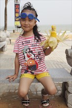 Young Chinese girl with swimming goggles and corn on the cob
