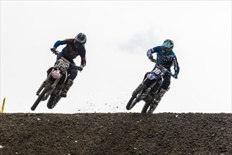 Two motorcyclists on motocross bikes riding on a dirt track