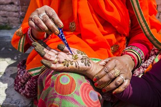 An indian woman is painting a hand with henna