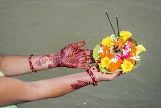 A pair of henna painted hands are holding a deepak