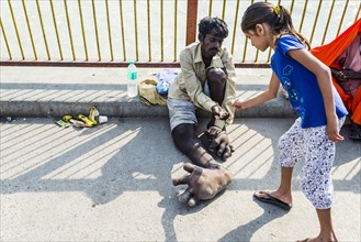 A beggar with Elephantiasis at his feet is receiving some money from a girl at Harki Pauri Ghat at the holy river Ganges
