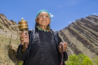 An old Ladakhi woman is turning a prayer wheel