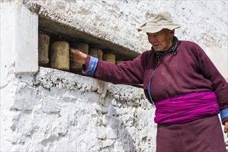 An old Ladakhi man is turning a prayer wheel at a wall of Hemis Gompa