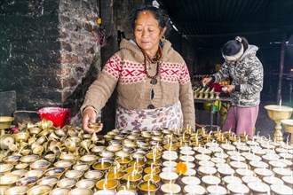 A woman is arranging butter lamps at a temple in Boudha