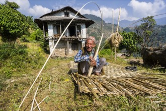 Man building a woven bamboo fence to be used as a wall in front of his farmers house