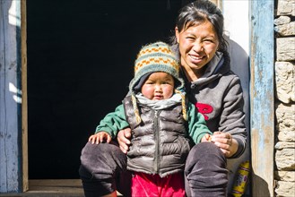 Portrait of a smiling young nepali mother with her child sitting in a doorway