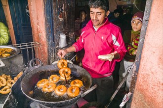 A man is frying doughnuts in a big pan for the typical nepali breakfast
