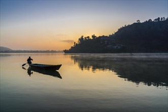 Man paddling a boat across Phewa Lake at sunrise