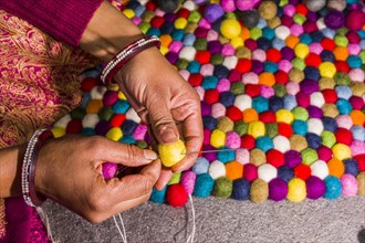 Hands of a woman are producing a carpet from felt balls