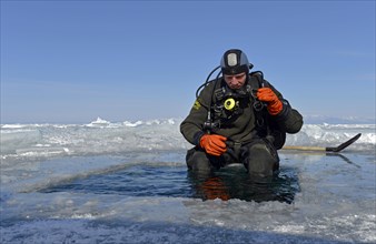 Ice diver by an ice hole preparing to dive