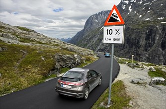 Cars by a warning sign in front of a steep slope