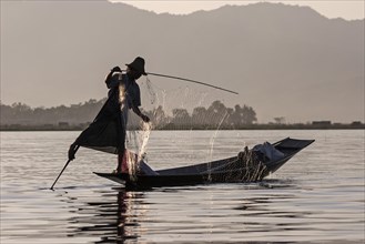 Traditional leg rower in a boat with fishing net in the backlight