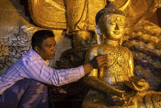Local man adding gold leaf to seated Buddha figure