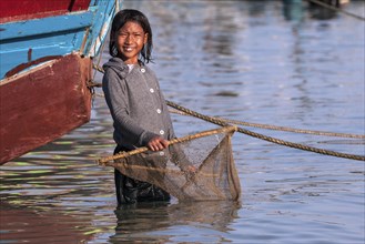 Local girl with a small fishing net in the water at the beach of the fishing village Ngapali