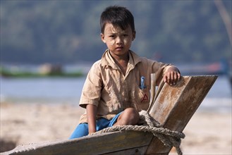 Local boy with Thanaka paste on his face sitting on the bow of a fishing boat