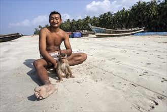 Local man sitting with a monkey on a leash on the beach of the fishing village Ngapali