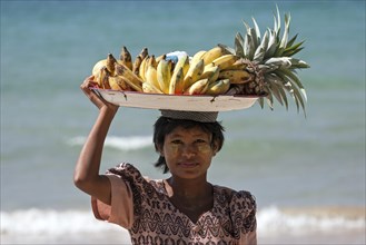 Native woman with a bowl of bananas on her head and Thanaka paste on her face