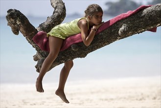 Local girl lying on tree branch on Beau Vallon beach