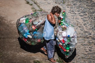 Elderly woman carrying bags with plastic bottles to sell for recycling
