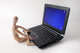Wooden doll sitting in front of a laptop