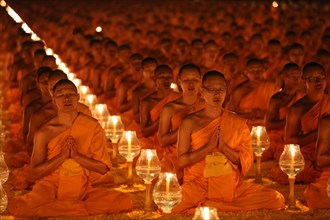 Monks sitting in rows praying and meditating by candlelight