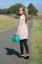 Young brunette woman holding a petrol can walking on a country road