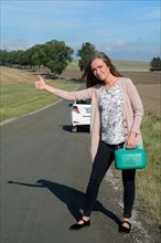 Young brunette woman holding a petrol can hitchhiking on an empty country road