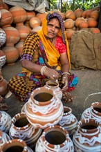 A woman painting pots and water jugs at a pottery stall in Jaipur