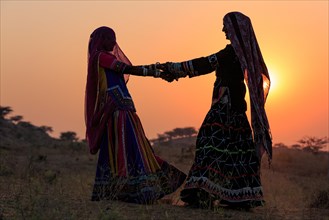 Two young women in dresses dancing in front of the setting sun