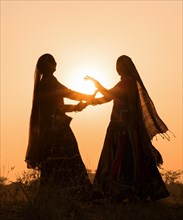 Two women in dresses dancing in front of the setting sun