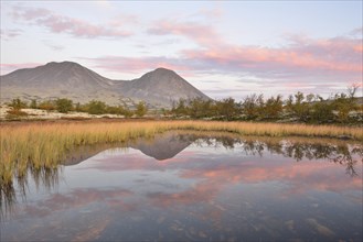 Red sky in the morning above the peaks of the Stygghoin or Stygghoin mountain group reflected in a small lake