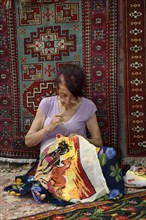 Woman doing embroidery in front of an Armenian carpet