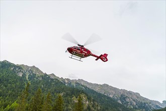 Red Aiut Alpin rescue helicopter I-AIUT taking off from meadow