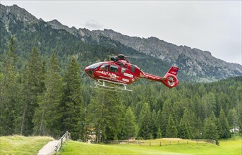 Red Aiut Alpin rescue helicopter I-AIUT taking off from meadow