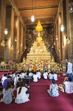 Buddhist monk speaking to believers in front of Seated Buddha in Wat Pho temple