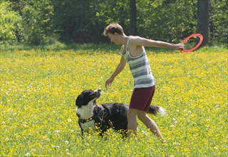 Young man playing frisbee with dog in meadow
