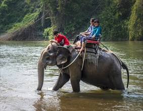 Two tourists riding elephant in water with mahout
