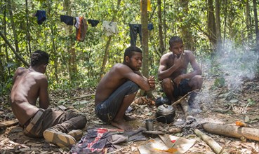 Three young aboriginal Orang Asil men sitting on the ground in the jungle