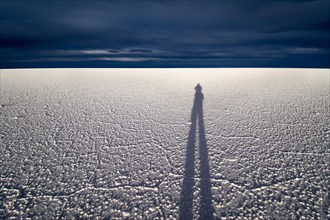 Shadow of man on salt flat in front of dark clouds