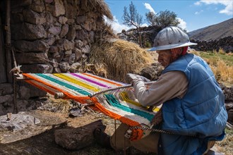 Old Indio man with helmet weaving a colorful rug with a simple loom