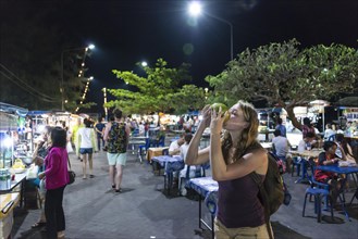 Female tourist drinking from a coconut at a night market