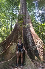 Young woman standing in front of a large forest giant in the jungle