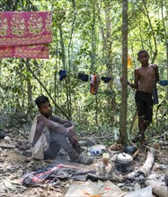 Two young men of the Orang Asil tribe sitting on the ground in the jungle and making tea